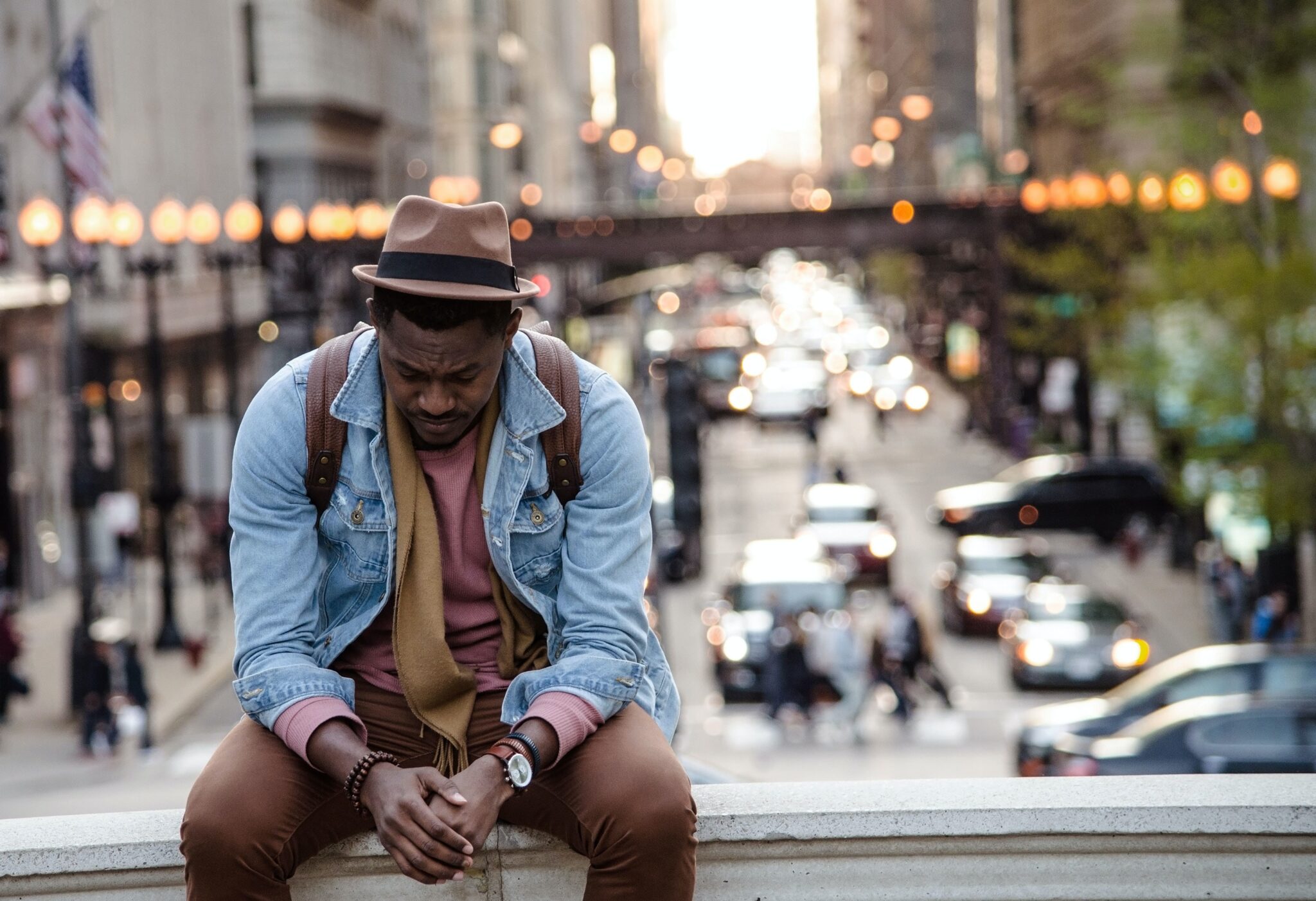 A black man sits on the railing of a bridge. He looks pensive.