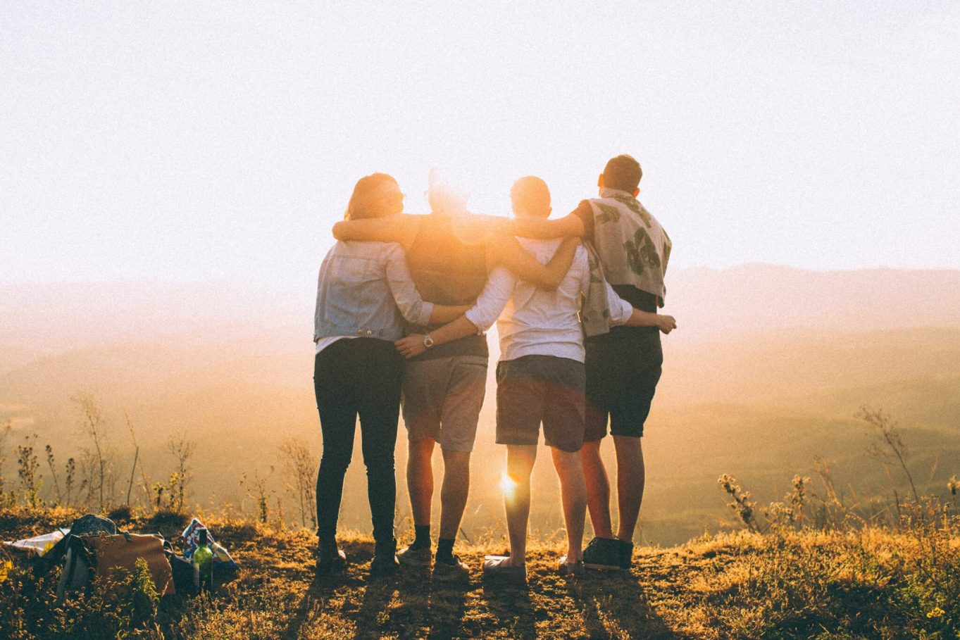 Four people share a hug. Their backs are facing the camera. Photo by Helena Lopes on Unsplash.